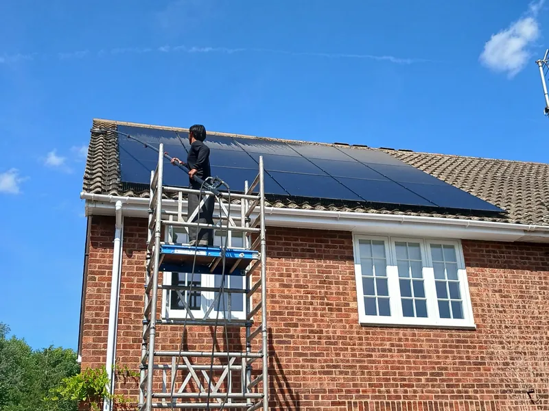 Technician cleaning solar panels on a residential roof